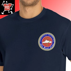 May include: A navy blue t-shirt with a circular patch featuring a red and white boat on a blue background. The patch has the text "Officially Traveling The Great Loop" in a gold circle with a rope border.