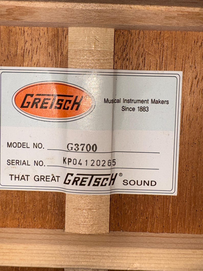 May include: A close-up of a label from a Gretsch musical instrument. The label includes the Gretsch logo, model number G3700, and serial number KP04120265. The text reads "Musical Instrument Makers Since 1883" and "That Great Gretsch Sound."