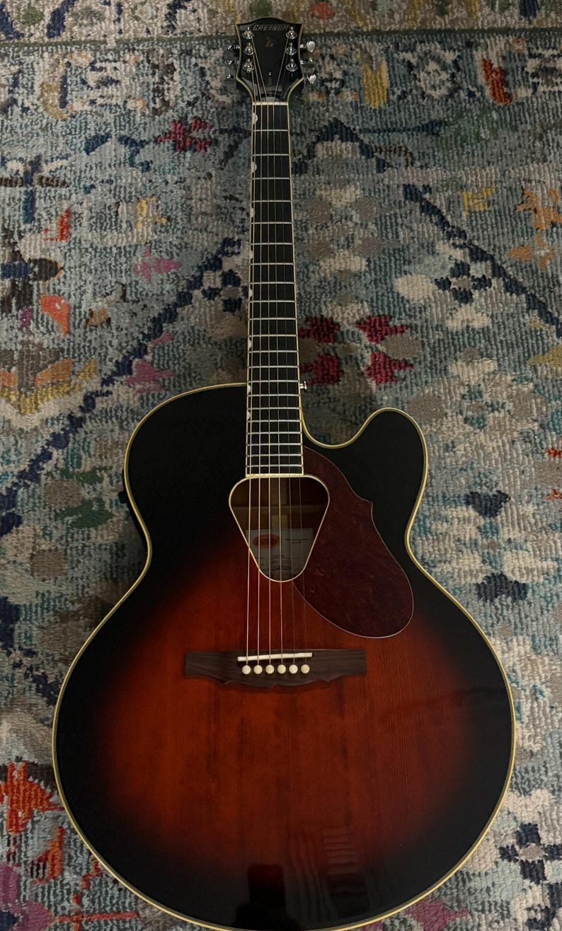 May include: Acoustic-electric guitar with a sunburst finish, featuring a black top and a brown body. The guitar has a cutaway design, a pickguard, and six strings. The headstock has the brand name.