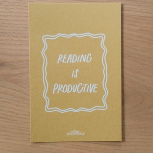 May include: A yellow card with white text that reads "Reading is Productive" inside a white decorative frame. The text "Tiny Bookshelf" is at the bottom of the card.
