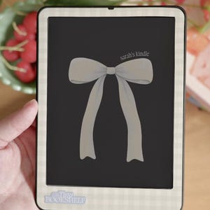 Könnte beinhalten: Ein Kindle E-Reader mit einem schwarzen Bildschirm mit einer hellgrauen Schleifenillustration. Der E-Reader hat einen weiß-hellgrünen Vichy-Rand und den Text "sarah's kindle". Der Boden des E-Readers trägt den Text "Tiny Bookshelf".