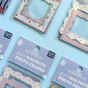 May include: Mini magnetic photo frames in packs of four. The frames have scalloped edges and various patterns, including polka dots, strawberries, and gingham. The text "The Tiny Bookshelf mini MAGNETIC PHOTO FRAMES" is printed on the packaging.