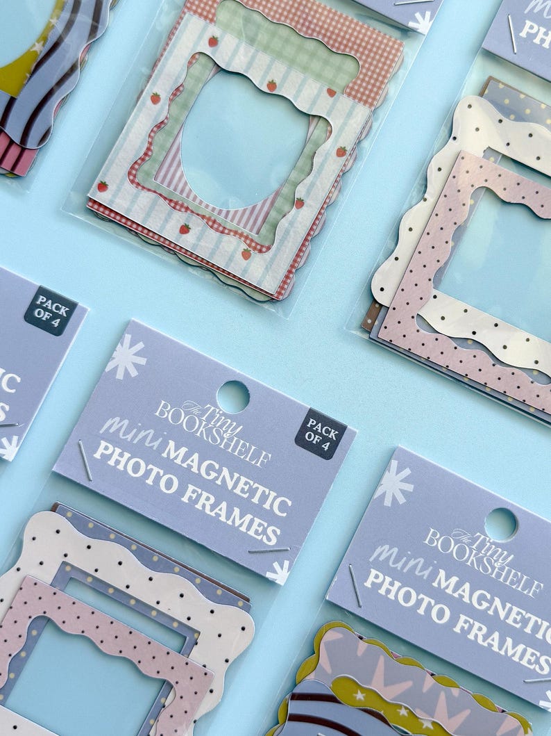 May include: Mini magnetic photo frames in packs of four. The frames have scalloped edges and various patterns, including polka dots, strawberries, and gingham. The text "The Tiny Bookshelf mini MAGNETIC PHOTO FRAMES" is printed on the packaging.