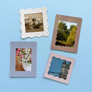May include: Four decorative picture frames with scalloped edges and polka dots. The frames are in white, brown, light blue, and pink. The frames contain images of a sculpture, a landscape, a bouquet of flowers, and a building.