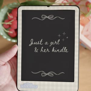 May include: A black and white e-reader with a white and black checkered border. The screen displays the text "Just a girl & her kindle" in white. The e-reader has a small sticker that says "Tiny Bookshelf".