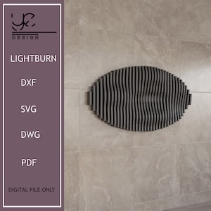 Puede incluir: Una decoración de pared ovalada de color negro y gris hecha de listones verticales delgados. Los listones están dispuestos en forma de onda. La decoración está montada en una pared de azulejos beige claro. El texto "LIGHTBURN" es visible en la imagen.