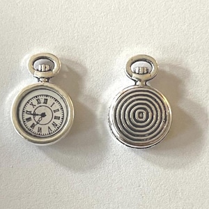 May include: Two silver-coloured pocket watch charms. One charm features a white clock face with black Roman numerals and hands. The other charm has a spiral design on the back. Both charms have a loop at the top for attaching to jewellery.