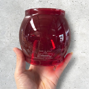 May include: A red glass Coleman lantern globe. The globe is a replacement part, with the text "MADE IN U.S.A. FOR Coleman" and "REPLACEMENT NO. 690A051 C-32" printed on the side.