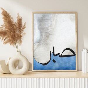 K&ouml;nnte beinhalten: Ein gerahmter Druck mit einem blauen und wei&szlig;en Aquarellhintergrund und schwarzer arabischer Kalligraphie, die "حب" lautet, was im Deutschen "Liebe" bedeutet.