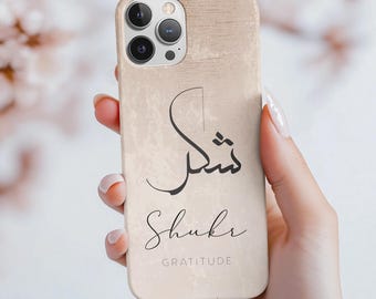 May include: A beige phone case with a wood grain texture. The case features a black Arabic calligraphy design that says "Shukr" and the word "Gratitude" in English.