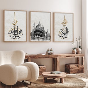 Puede incluir: Tres impresiones enmarcadas con caligrafía negra y dorada y una ilustración de una mezquita. Las impresiones están colgadas en una pared blanca sobre una mesa de madera con una silla blanca y un taburete de madera.