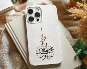 May include: White phone case with a gold and black Arabic calligraphy design. The design features the phrase "In the name of Allah, the Most Gracious, the Most Merciful".
