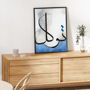 K&ouml;nnte beinhalten: Ein gerahmter Schwarzwei&szlig;-Kalligrafie-Kunstdruck mit blauen Akzenten. Der Druck zeigt arabische Schrift auf silbernem Hintergrund mit einem blauen Aquarell-Wasch unten.