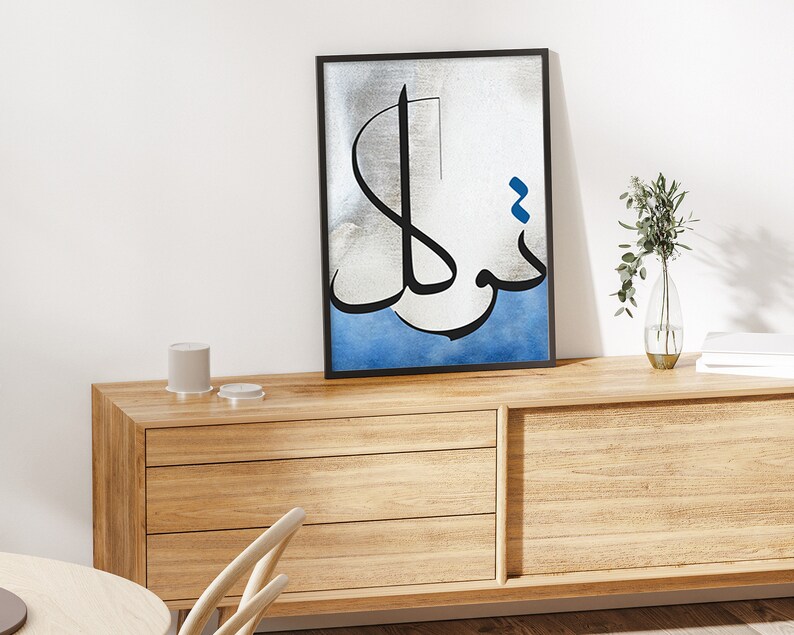K&ouml;nnte beinhalten: Ein gerahmter Schwarzwei&szlig;-Kalligrafie-Kunstdruck mit blauen Akzenten. Der Druck zeigt arabische Schrift auf silbernem Hintergrund mit einem blauen Aquarell-Wasch unten.
