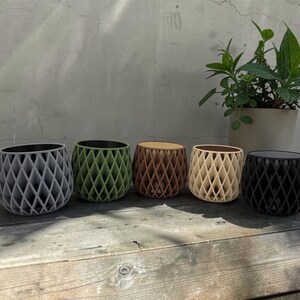 May include: Five small, round planters arranged in a row, each featuring a distinct lattice-style exterior pattern. The planters are colored in light gray, olive green, brown, cream, and black, with smooth, dark-colored interior liners visible.