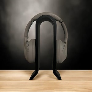 May include: A black headphone stand with a pair of gray headphones resting on it. The stand is on a light brown wooden surface.