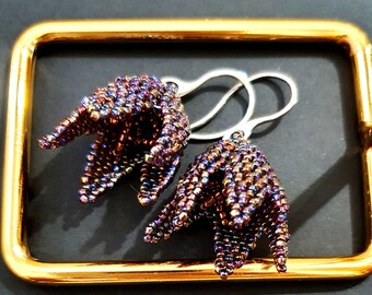 May include: A pair of iridescent purple and brown beaded earrings with silver hooks. The earrings are shaped like a flower with five petals.