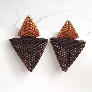 Könnte beinhalten: Ein Paar geometrische Dreiecksohrringe in einem braunen und kupferfarbenen Farbschema. Die Ohrringe bestehen aus kleinen Perlen und haben ein modernes, minimalistisches Design.