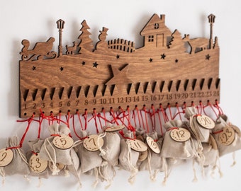 Può includere: Calendario dell'Avvento in legno con un design di villaggio natalizio. Ha 24 sacchetti numerati che pendono dalla parte inferiore. Il calendario è in legno marrone e ha uno spago rosso.