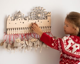 Op de afbeelding: Een houten adventskalender in de vorm van een kermis met een reuzenrad, een draaimolen en een kerstboom. De kalender heeft 24 genummerde vakjes, elk met een klein stoffen zakje eraan hangend. Een jong meisje reikt naar een van de zakjes.