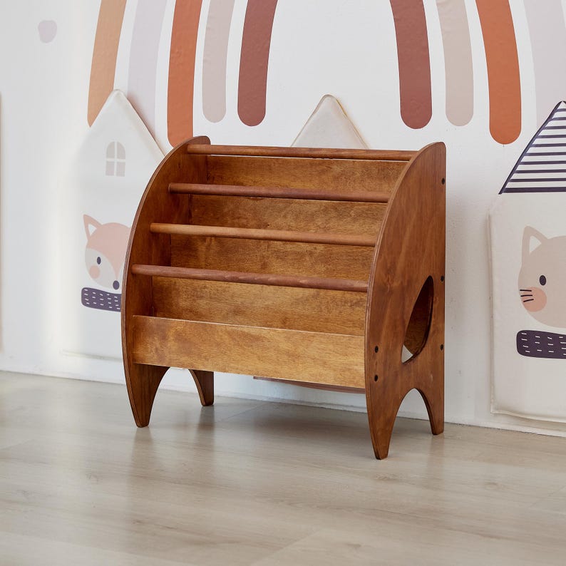 K&ouml;nnte beinhalten: Ein mittelbraunes Holzregal mit nach vorne gerichtetem Design und drei horizontalen Stangen zur Aufbewahrung von B&uuml;chern. Das M&ouml;belst&uuml;ck hat geschwungene Seitenteile mit bogenf&ouml;rmigen Ausschnitten an der Basis und eine glatte Holzmaserung.