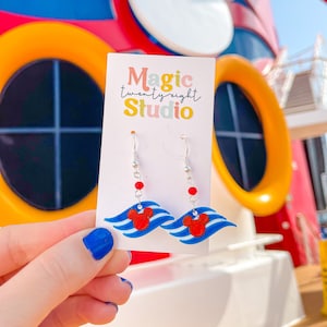 May include: A pair of silver dangle earrings with red and blue Mickey Mouse themed charms. The charms feature a red Mickey Mouse head on a blue and white striped wave design. The earrings are displayed on a white card with the text "Magic twenty eight Studio".