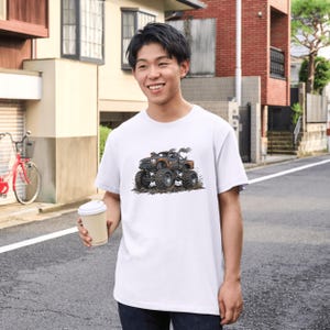 May include: White t-shirt featuring a detailed graphic of a monster truck with large tires, smoke, and the word "BEAST". The truck is brown and black, set against a dirt background. The shirt is short-sleeved.