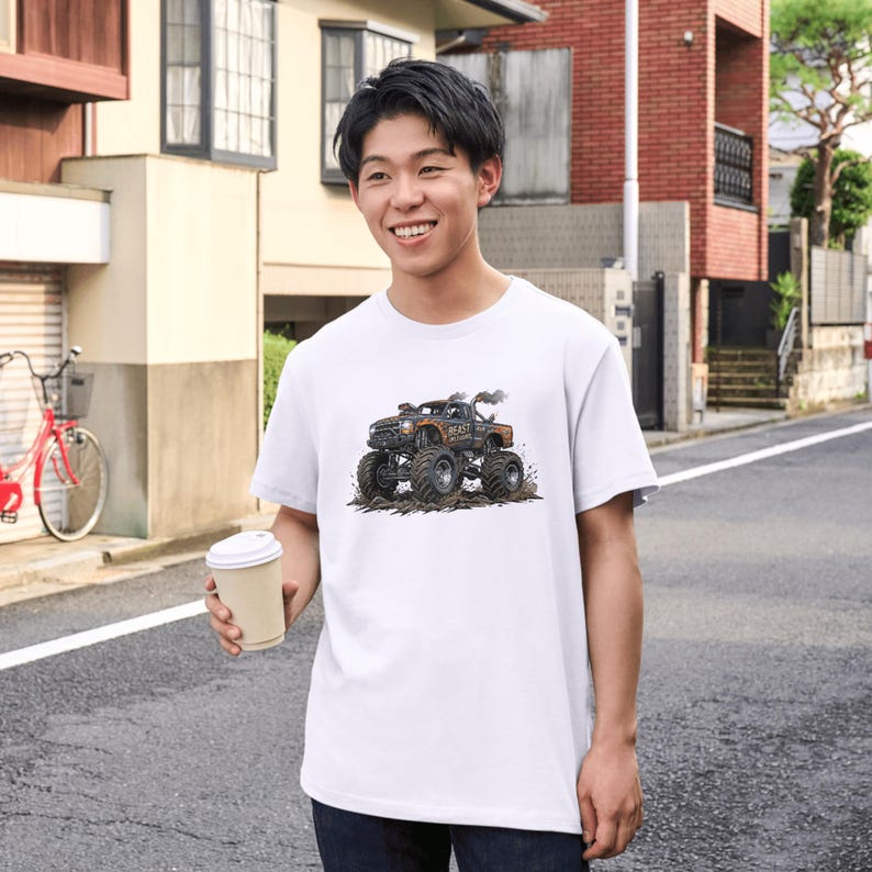 May include: White t-shirt featuring a detailed graphic of a monster truck with large tires, smoke, and the word "BEAST". The truck is brown and black, set against a dirt background. The shirt is short-sleeved.