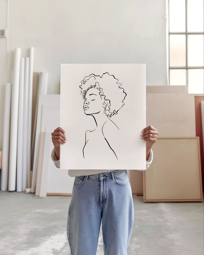 An artist studio room interior. A woman artist holds up a poster in front of her face. Concrete floor. Paper rolls and blank art canvas. Large warehouse windows, sunlight streams in
