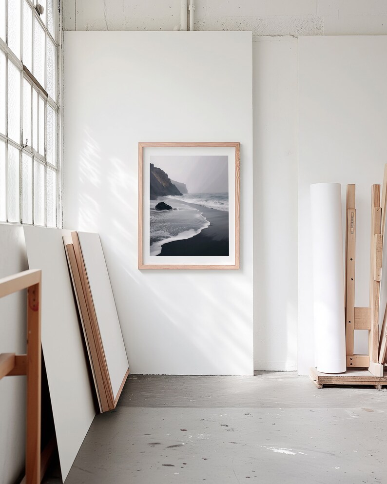 A blank thin oak wood frame mockup, in a minimal bright artist studio, with rolls of art paper and blank canvas