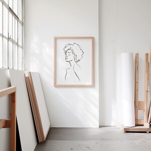 A blank thin oak wood frame mockup, in a minimal bright artist studio, with rolls of art paper and blank canvas