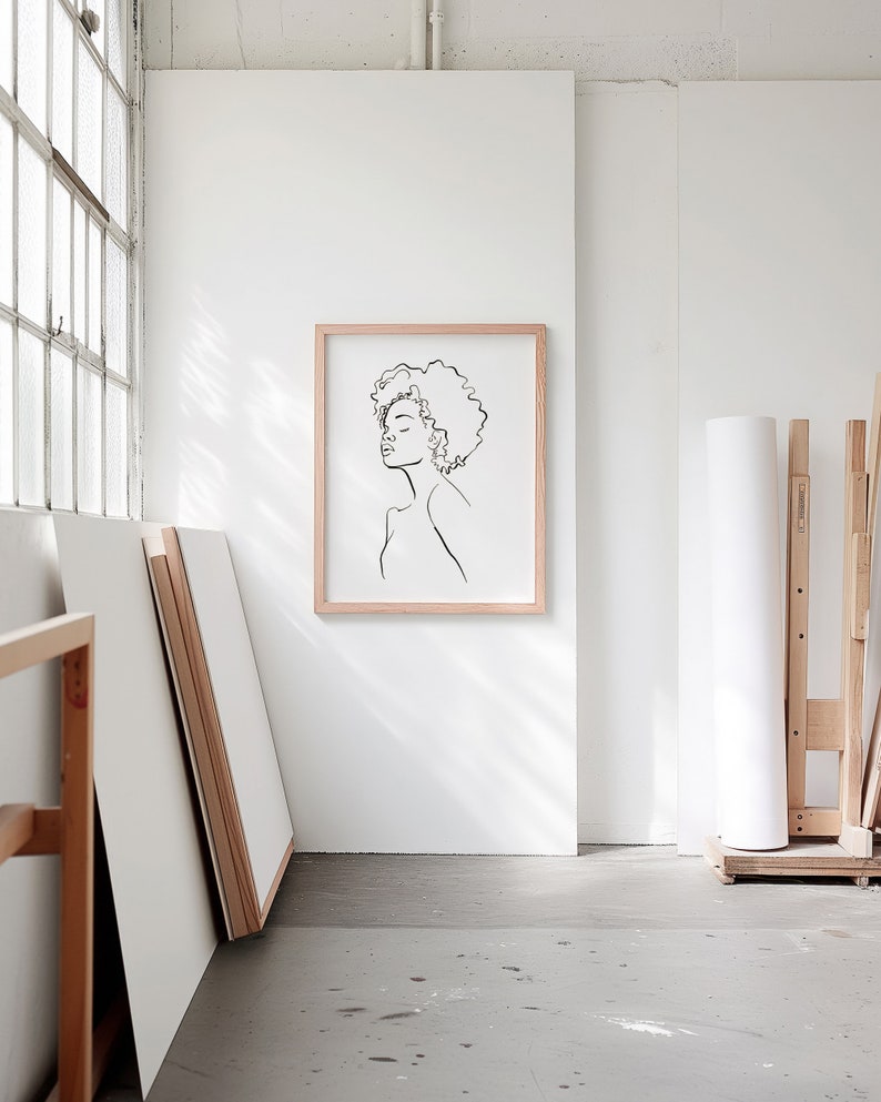 A blank thin oak wood frame mockup, in a minimal bright artist studio, with rolls of art paper and blank canvas