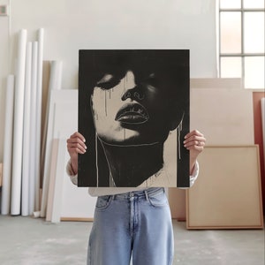 An artist studio room interior. A woman artist holds up a poster in front of her face. Concrete floor. Paper rolls and blank art canvas. Large warehouse windows, sunlight streams in