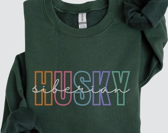 Op de afbeelding: Bosgroen sweatshirt met de tekst "HUSKY" in regenboogkleuren en "siberian" in wit schrift eronder.
