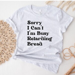 Könnte beinhalten: Ein graues T-Shirt mit dem Text "Sorry, I Can't I'm Busy Retarding Bread" in Schwarz gedruckt.