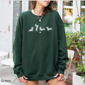 May include: Forest green sweatshirt with a white graphic of five dachshund dogs in a line, with a heart between the second and third dog.
