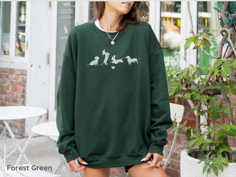 May include: Forest green sweatshirt with a white graphic of five dachshund dogs in a line, with a heart between the second and third dog.