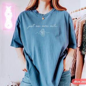May include: Blue jean-colored t-shirt with the text "just one more mile" and a line drawing of a running shoe. The shirt is a comfortable, oversized fit.
