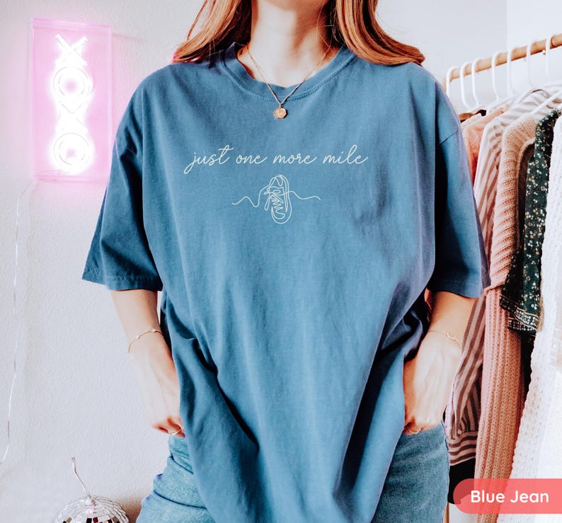 May include: Blue jean-colored t-shirt with the text "just one more mile" and a line drawing of a running shoe. The shirt is a comfortable, oversized fit.