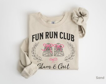 May include: A beige sweatshirt with the text "Fun Run Club" and a graphic of two running shoes with pink laces. The text "Glam & Grit" is below the graphic.