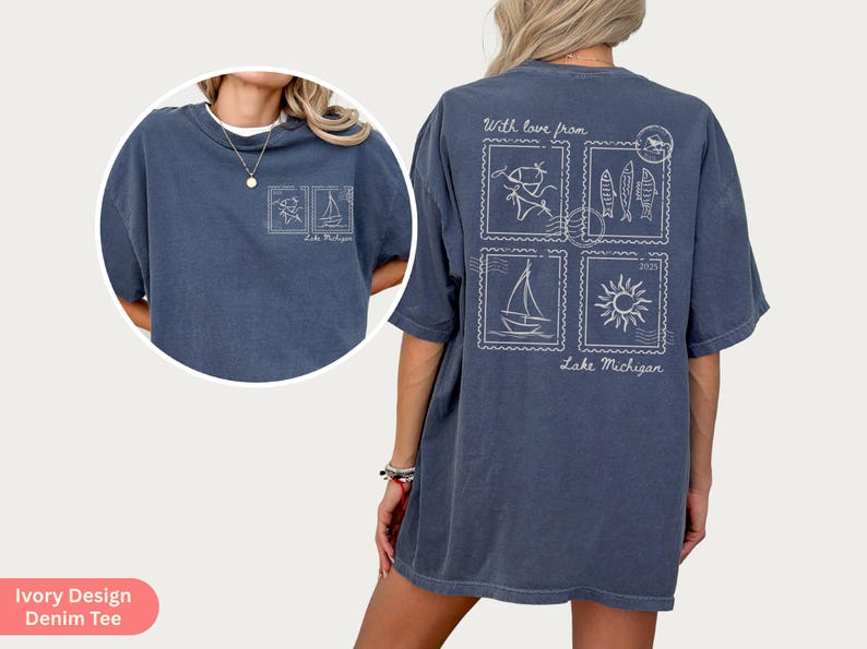 May include: A denim blue tee shirt with a white graphic design. The design includes four postage stamp-like images with drawings of fish, a sailboat, a sun, and a person fishing. The text "With love from Lake Michigan" is also included.