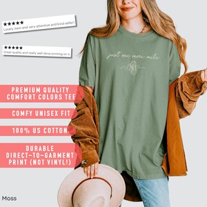 May include: A moss green unisex t-shirt with the text "just one more mile" and a line drawing of a shoe. The shirt is made of 100% US cotton and has a comfy fit. The print is durable and direct-to-garment.