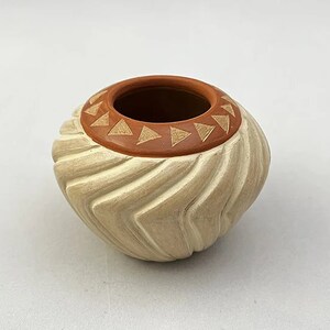 May include: A small, white ceramic pot with a brown rim and a geometric design. The pot has a wavy, textured surface.
