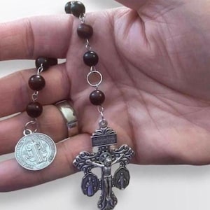 May include: A rosary with dark brown wooden beads and silver-toned metal components. The rosary features a crucifix with a detailed depiction of Jesus and two smaller figures, and a round medal with an image of a saint.