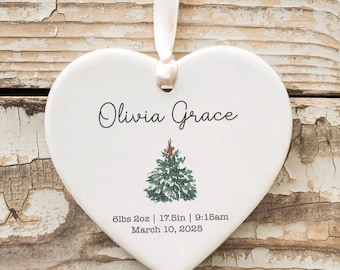 May include: White ceramic heart ornament with a green Christmas tree and the text "Olivia Grace 6lbs 2oz | 17.5in | 9:15am March 10, 2023"