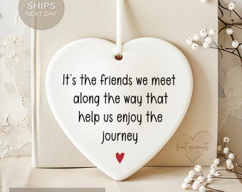 May include: White ceramic heart-shaped ornament with the text "It's the friends we meet along the way that help us enjoy the journey" in black lettering. A small red heart is at the bottom of the ornament.