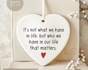May include: White ceramic heart-shaped ornament with a black inscription that reads "It's not what we have in life, but who we have in our life that matters." A small red heart is at the bottom of the ornament.
