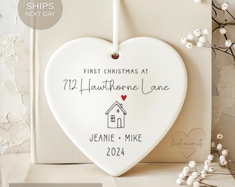 May include: White ceramic heart ornament with the text "First Christmas at 712 Hawthorne Lane" and a small house illustration. Below the house is the text "Jeanie + Mike 2024".