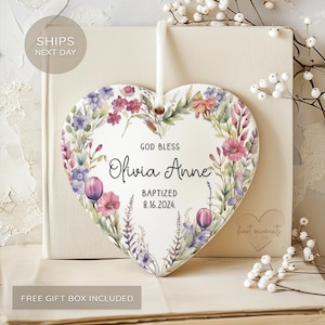 May include: White ceramic heart-shaped ornament with a watercolor floral design. The ornament features the text "God Bless Olivia Anne Baptized 8.16.2024."