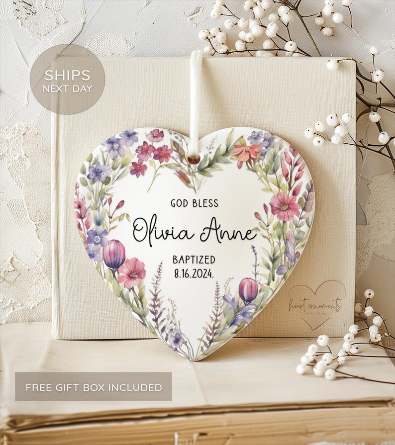 May include: White ceramic heart-shaped ornament with a watercolor floral design. The ornament features the text "God Bless Olivia Anne Baptized 8.16.2024."